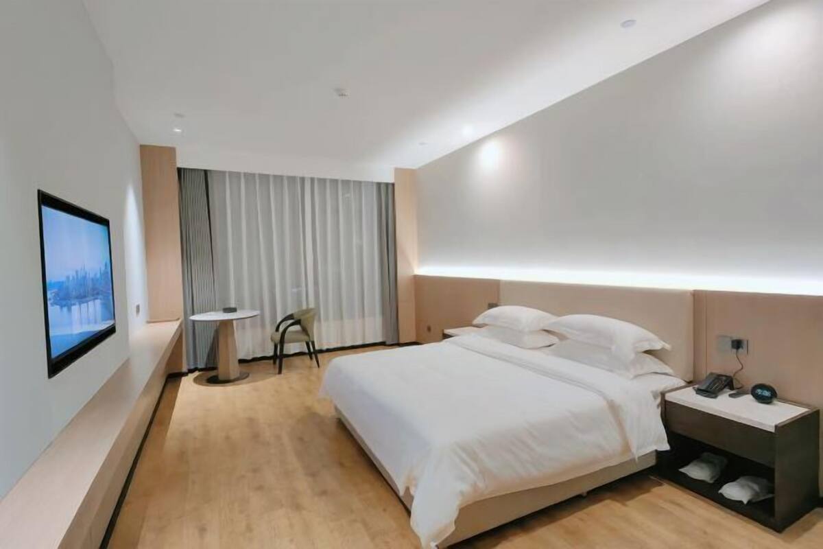 A modern hotel room with a large bed, a bedside table with a phone and charger, a small round table, and a TV mounted on the wall.