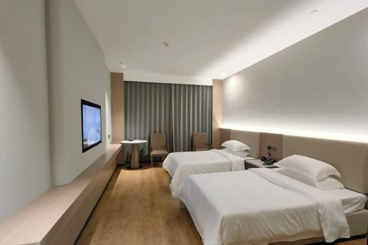 A hotel room with two beds, a TV on the wall, a desk with a chair, and a curtain.