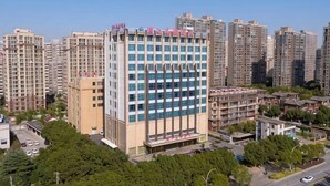 A high-rise building with multiple floors, surrounded by other high-rise buildings, and a clear sky. - Riverside Garden Hotel (Taicang)