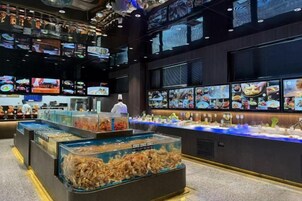 Exhibición de mariscos con diversos recipientes y un panel de menú digital al fondo.