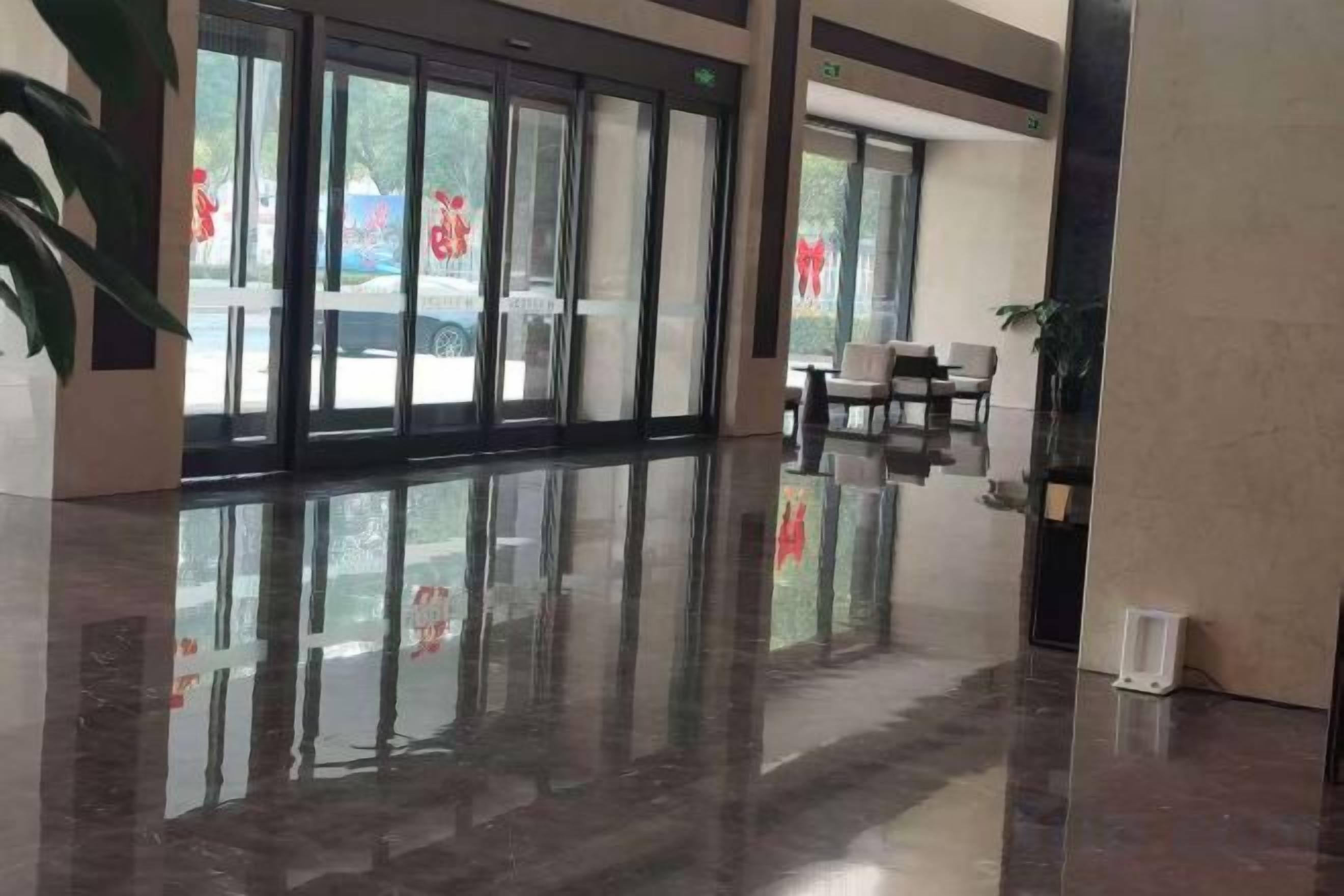 Un hall de hotel con piso reflectante, ventanas amplias y un área de descanso con sillas.