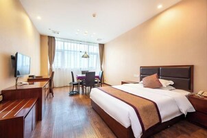 Una habitación de hotel con una cama grande, un escritorio con silla, televisor y ventana con cortinas.
