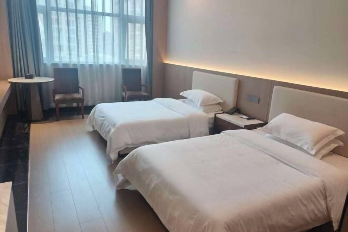 A hotel room with two beds, a small table, two chairs, and a window with curtains.