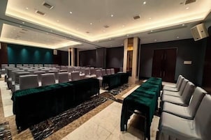 Un salón de conferencias con filas de sillas, una mesa larga y una zona de escenario.