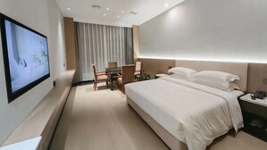 A hotel room with a bed, a desk, a chair, a TV mounted on the wall, and a window with curtains. - Riverside Garden Hotel (Taicang)