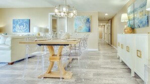 Un comedor con una mesa de madera y sillas transparentes, un sofá y obras de arte en las paredes.