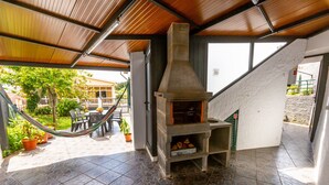 Un patio con suelo de piedra, una estufa de leña, mobiliario de exterior y una hamaca.