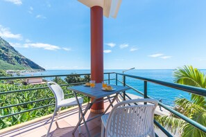 A balcony with a table, chairs, and a view of the sea.