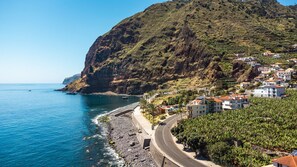 Une ville côtière où une route serpente le long de la plage, avec des maisons aux toits couverts de tuiles rouges et une colline abrupte.