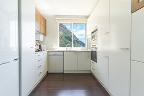 Cocina compacta con armarios blancos, lavavajillas, estufa y ventana con vista a la montaña.