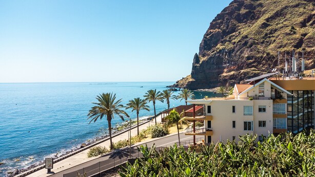 A coastal building with a balcony overlooking the sea, a paved walkway, and palm trees. - Sunny Side by Atlantic Holiday (Madalena do Mar)