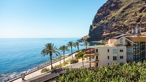 A coastal building with a balcony overlooking the sea, a paved walkway, and palm trees. - Sunny Side by Atlantic Holiday (Madalena do Mar)
