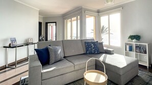 A modern living room with a grey sofa, a wooden side table, and a bookshelf. - Sunny Side by Atlantic Holiday (Madalena do Mar)