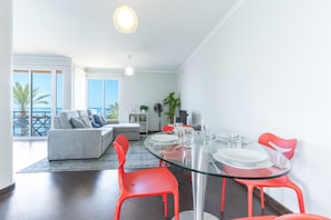 A modern living room with a glass dining table, red chairs, and a grey sofa. - Sunny Side by Atlantic Holiday (Madalena do Mar)