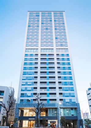 A tall, modern hotel with a grid of windows and balconies, featuring a prominent entrance with signage.