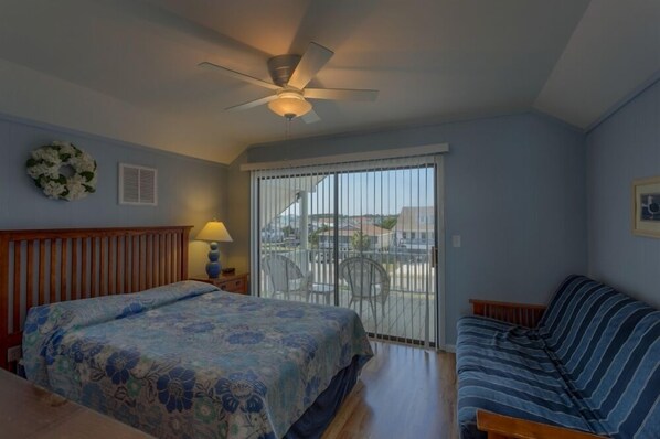 Ein Schlafzimmer mit einem Bett, einer Couch, einem Deckenventilator, einem Fenster mit Jalousien und Blick ins Freie.