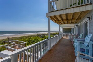 Eine Holzterrasse mit weißen Geländern mit Blick auf einen Strand.