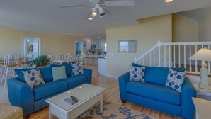 A spacious living area with two blue sofas, a white coffee table, and a ceiling fan. - A Beach Haven - Oceanfront Home w/Private Pool and Offers Early Check-In/Late Check-Out! (Holden Beach)