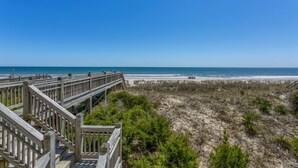 Une promenade en bois qui mène à une plage bordée de dunes de sable et d’une végétation clairsemée.