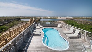Una terraza de madera con piscina, sillas de descanso y vistas a la playa y las dunas.