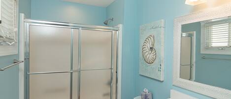 A bathroom with a glass-enclosed shower, a white sink, and a mirror with a decorative frame.