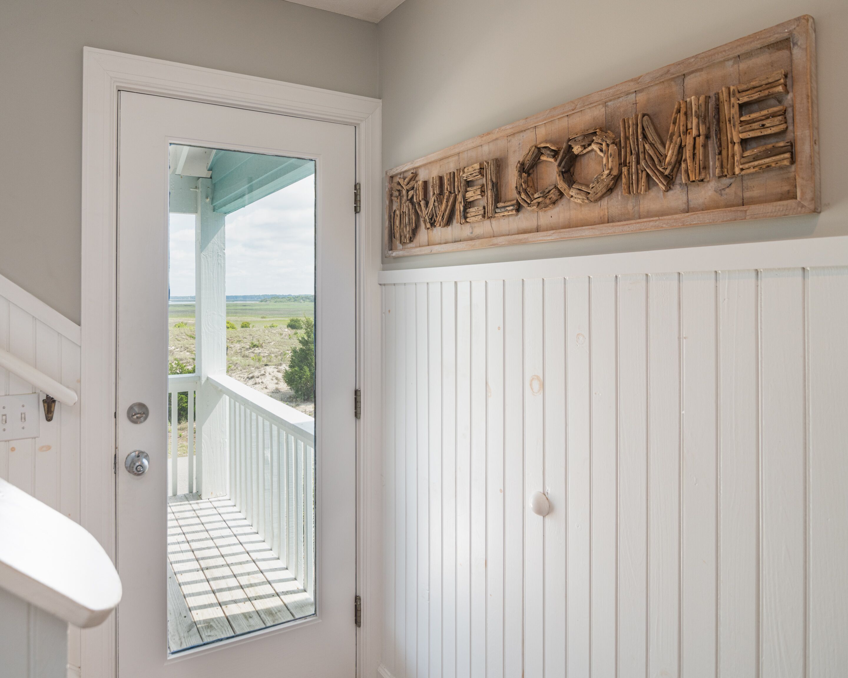 A white door with a view of a balcony and a welcome sign above it.