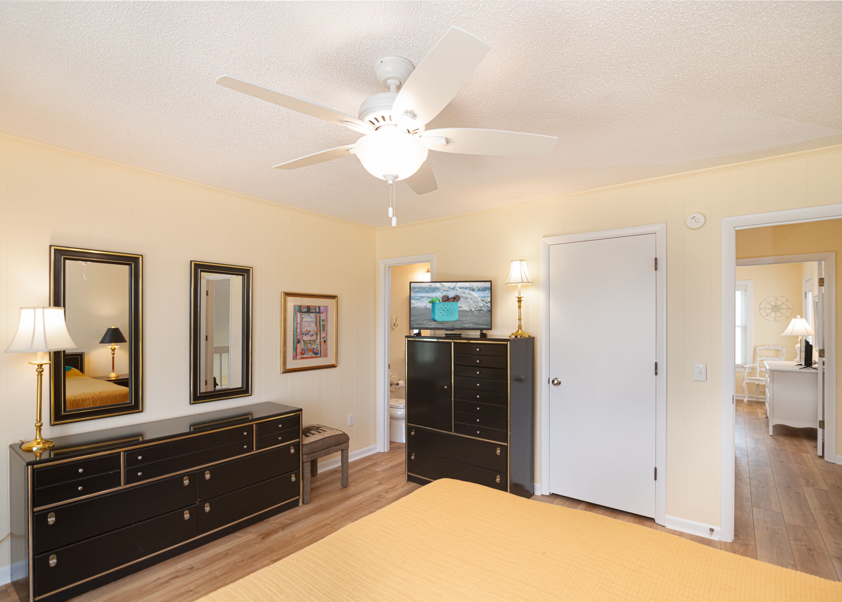 A bedroom with a bed, dresser, television, and a ceiling fan.