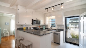 A kitchen with white cabinets, a central island with stools, a microwave, and a dishwasher.