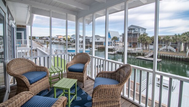 A covered outdoor deck with wicker furniture and a view of a marina.