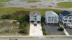 A coastal property with multiple buildings, a sandy driveway, and a view of the adjacent water body.