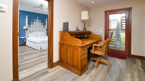 A bedroom with a bed, a wooden desk with a chair, a lamp, and a door leading to a balcony.