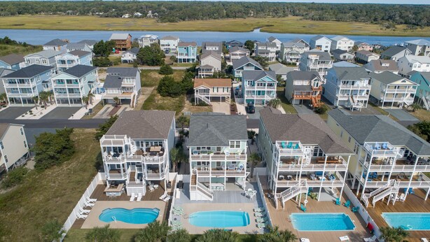 A residential area with multiple two-story houses featuring balconies, swimming pools, and a waterfront view. - Carolina in My Mind - Private pool, walking distance to beach, and more! (Holden Beach)