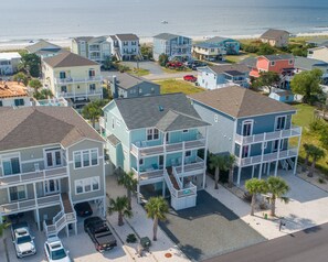 A coastal residential area with multi-story houses, a beach in the background, and a clear sky.