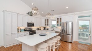 A modern kitchen with white cabinetry, stainless steel appliances, and a central island with bar stools. - Carolina in My Mind - Private pool, walking distance to beach, and more! (Holden Beach)