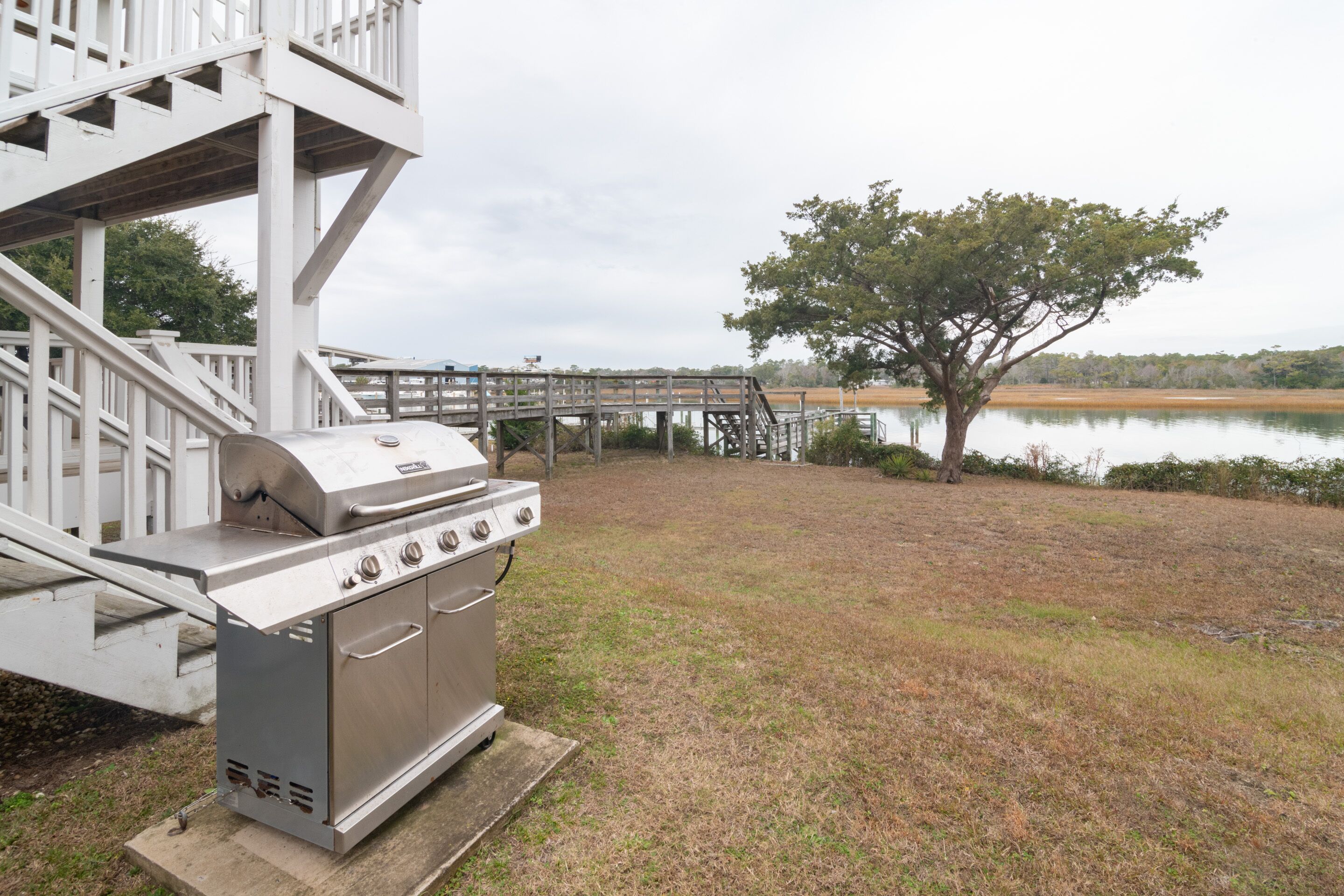 A barbecue grill in a backyard with a wooden deck and a view of a lake.