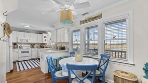 Una cocina con armarios blancos, una isla central y una zona de comedor con sillas azules y una mesa blanca.