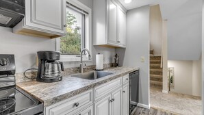 A modern kitchen with white cabinets, a granite countertop, a coffee maker, and a sink. - Modern Retreat with Stunning Views. Holiday Valley across the Street! Sleeps 8 (Ellicottville)