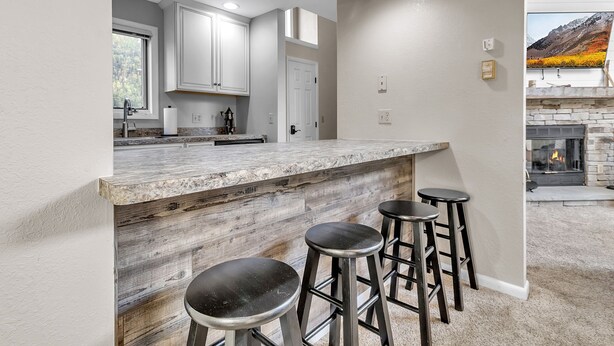 A modern kitchen with a marble countertop, white cabinets, and a stone fireplace. - Modern Retreat with Stunning Views. Holiday Valley across the Street! Sleeps 8 (Ellicottville)