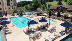 A hotel pool area with multiple pools, lounge chairs, umbrellas, and a view of a forested hillside. - Modern Retreat with Stunning Views. Holiday Valley across the Street! Sleeps 8 (Ellicottville)