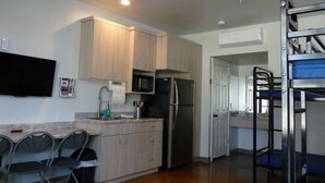 A compact kitchen with wooden cabinets, a stainless steel refrigerator, a microwave, and a sink. There are two chairs and a bunk bed in the room. - Bunkhouse 3A With Cold A/C (La Verkin)
