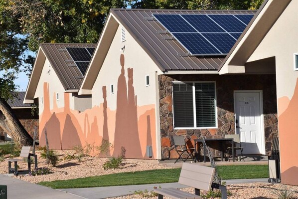 A residential building with solar panels on the roof, a stone facade, and a front porch with outdoor furniture.