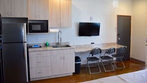 Una cocina moderna con refrigerador, microondas, pileta y un televisor de pantalla plana montado en la pared.