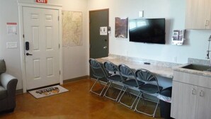 A compact kitchen with a dining area, a TV mounted above the counter, and an exit sign on the door. - Bunkhouse 10A In Peaceful Environment (La Verkin)