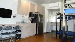 A compact kitchen with light wood cabinets, a stainless steel refrigerator, and a microwave. There is a small dining area with a table and chairs. - Bunkhouse 10A In Peaceful Environment (La Verkin)