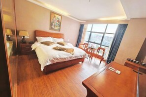 Une chambre d’hôtel avec un grand lit, un bureau en bois, une chaise, une table de chevet avec une lampe et une fenêtre avec des rideaux.
