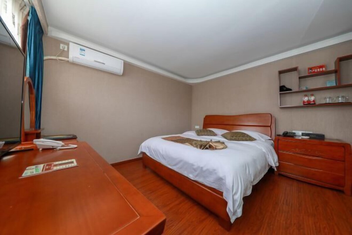Habitación de hotel ordenada con una cama de madera, una mesita de noche de madera, un escritorio pequeño y una estantería con artículos de aseo.