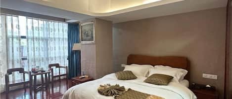 A hotel room with a large bed, a desk, chairs, and a view through the window.