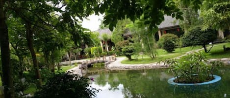 A tranquil garden with a pond, a bridge, and traditional-style buildings.