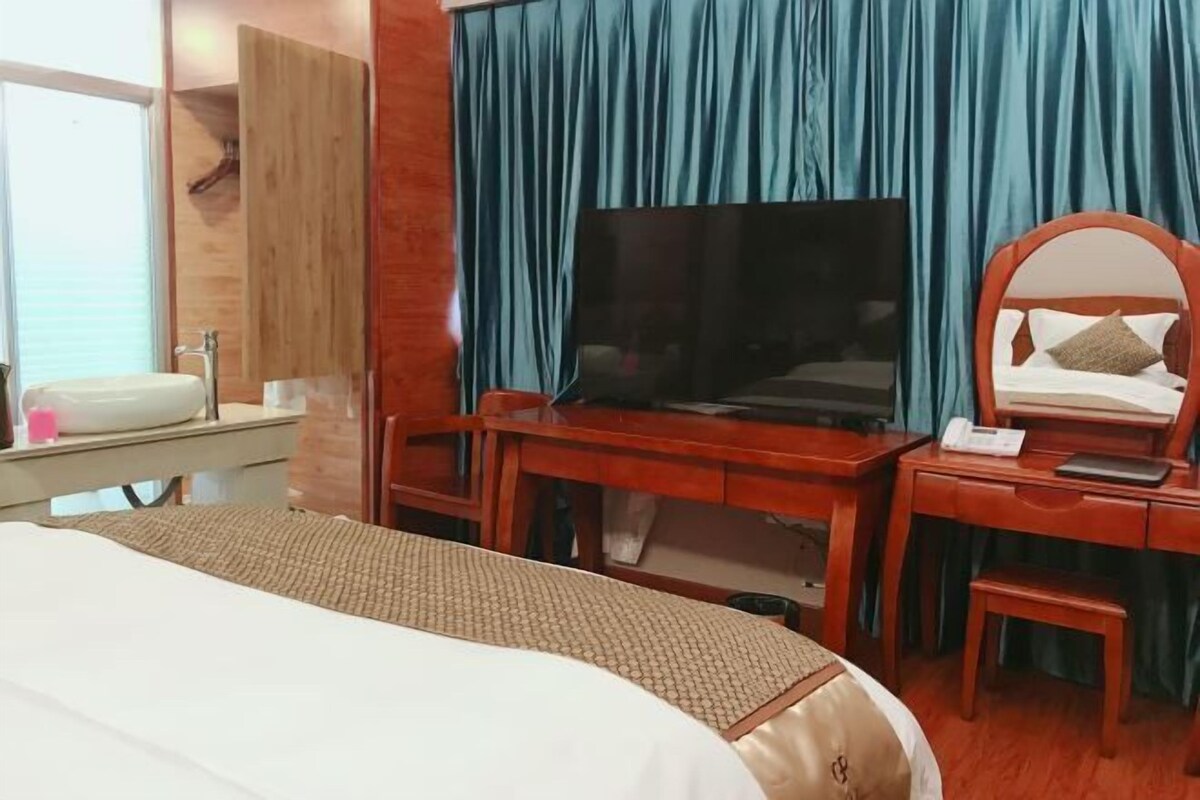 Una habitación de hotel con una cama, un escritorio con televisor, un espejo y una mesita.
