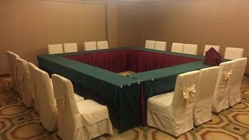 A conference room with a rectangular table surrounded by chairs, a red tablecloth, and white chair covers.